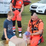 Na zdjęciu widzimy dwójkę wodnych ratowników medycznych, którzy pokazują dziecku jak prawidłowo wykonać resuscytację.