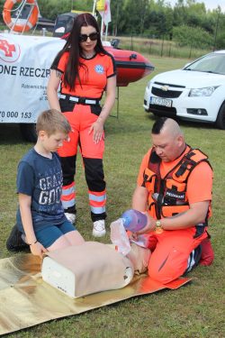 Na zdjęciu widzimy dwójkę wodnych ratowników medycznych, którzy pokazują dziecku jak prawidłowo wykonać resuscytację.