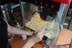 Na zdjęciu widzimy członkinię KGW w Sobiborze nakładającą popcorn z maszyny podczas Dnia Rodziny w Sobiborze.
