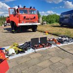 Na zdjęciu widzimy wóz strażacki OSP Orchówek oraz pokaz sprzętu pożarniczego wyłożony na kostce brukowej przed wozem.